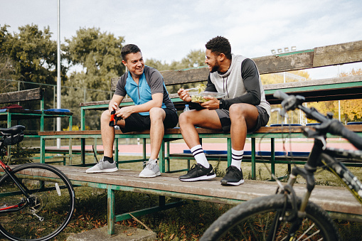 Two young male cyclists taking a break of bicycle ride in the city park talking.