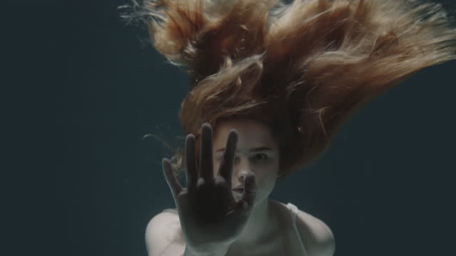 beautiful red-haired girl stopped underwater in front of the camera and froze