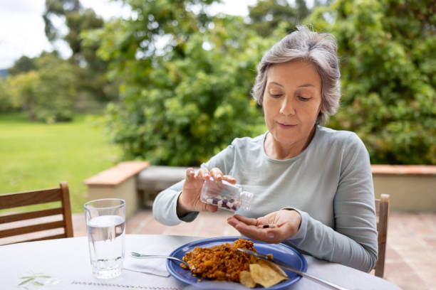 ältere frau, die ihre medikamente mit nahrung einnimmt, während sie zu mittag isst - aging process morning outdoors horizontal stock-fotos und bilder