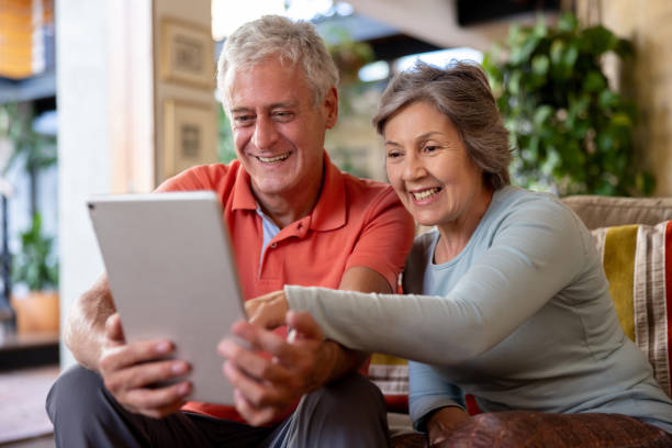 coppia anziana felice che guarda i social media su un tablet - ipad senior adult facebook sofa foto e immagini stock