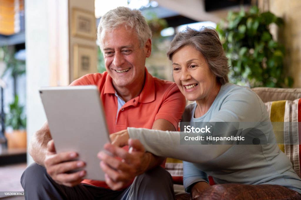 Happy senior couple looking at social media on a tablet computer Happy senior couple smiling at home while looking at social media on a tablet computer - lifestyle concepts Senior Adult Stock Photo