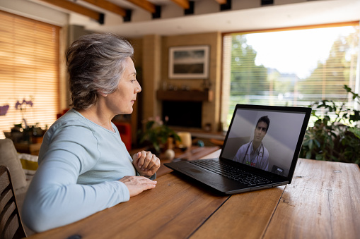 Latin American senior woman at home talking to her doctor on a video call using her laptop computer - telemedicine concepts