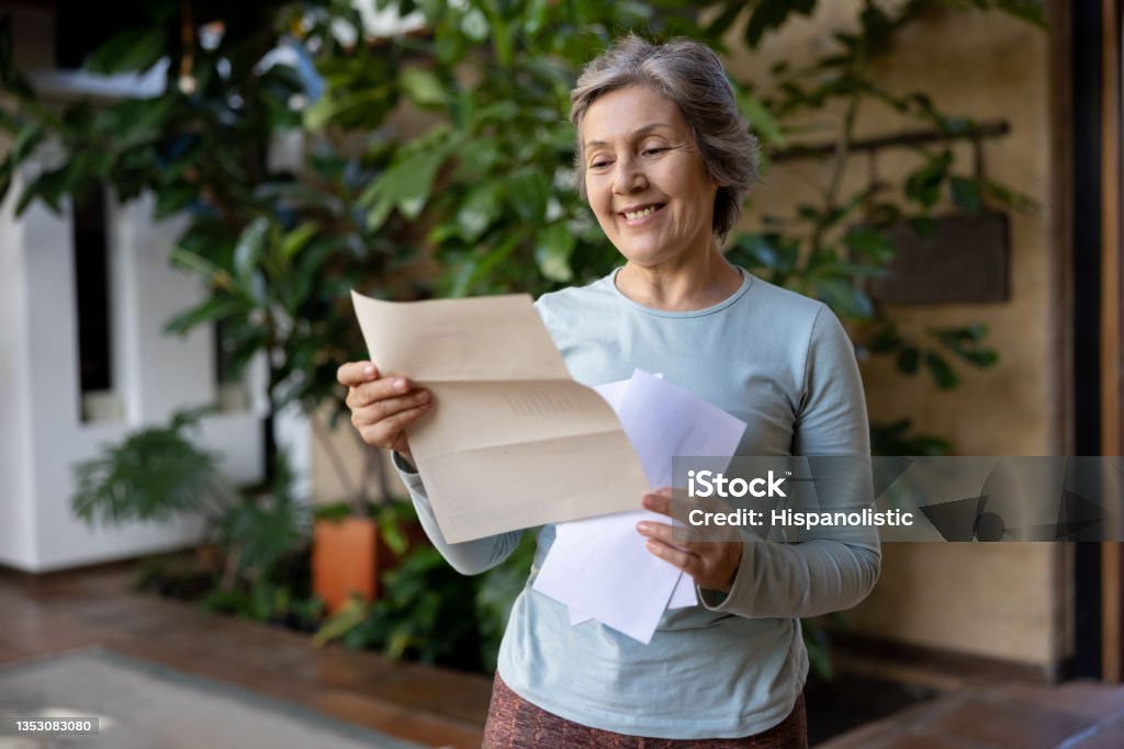 Happy senior woman reading a letter from the mail Happy senior woman at home reading a letter she got in the mail and smiling - domestic life concepts Senior Adult Stock Photo
