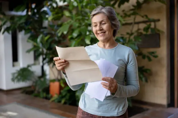 Happy senior woman at home reading a letter she got in the mail and smiling - domestic life concepts