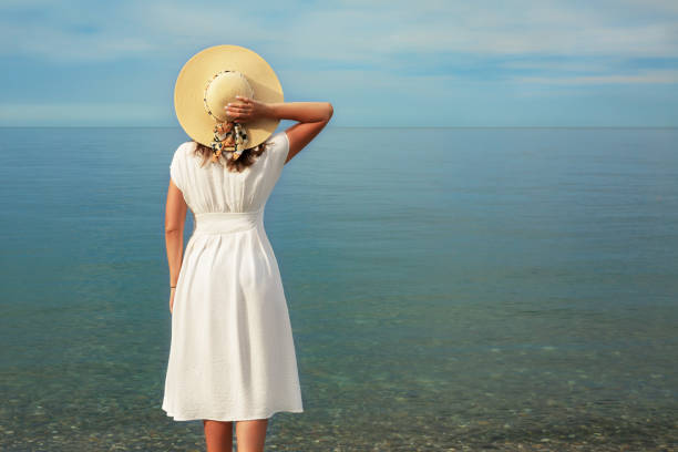 a girl in a white dress stands on the seashore. - white clothing imagens e fotografias de stock