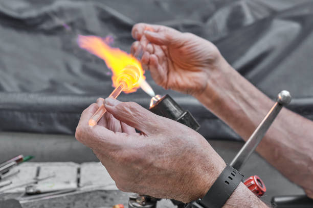 Process of artistic glass processing by burner flame. Hands of mature glassblower Process of artistic glass processing by burner flame. Hands of mature glassblower. Close up. Occupation concept hand blown glass stock pictures, royalty-free photos & images