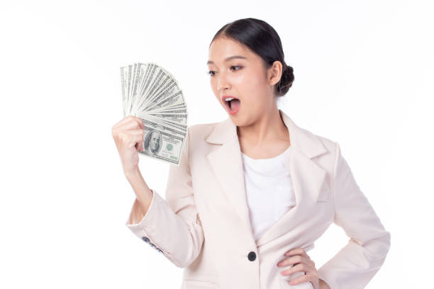 retrato de una hermosa joven asiática con traje sosteniendo billetes de dinero en dólares, servicio de cambio de moneda. plano de estudio aislado sobre fondo blanco. - currency women luxury wealth fotografías e imágenes de stock