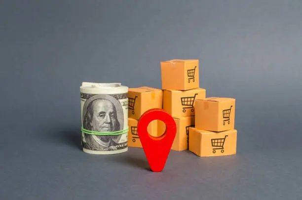 Photo of Roll bundle of dollars, red pointer location and cardboard boxes. Global market and business, import and export of goods and services. Local economy and production. Investments and project financing.