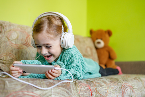 Laughing young child watching funny videos via smart phone and headphones