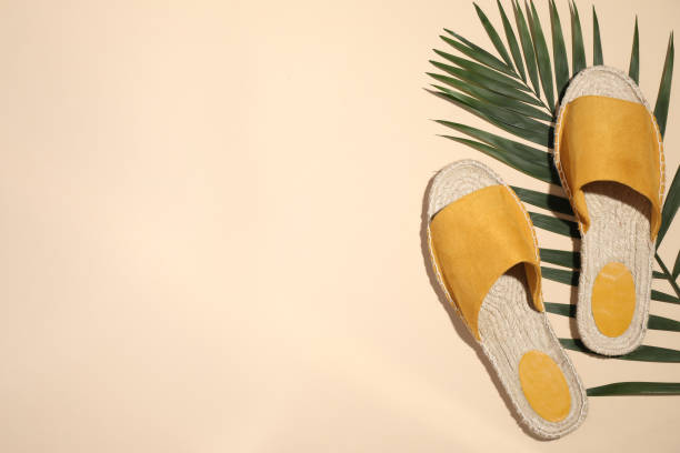 istock Slide shoes and palm leaf on beige background, flat lay with space for text. Beach accessory 1353098243
