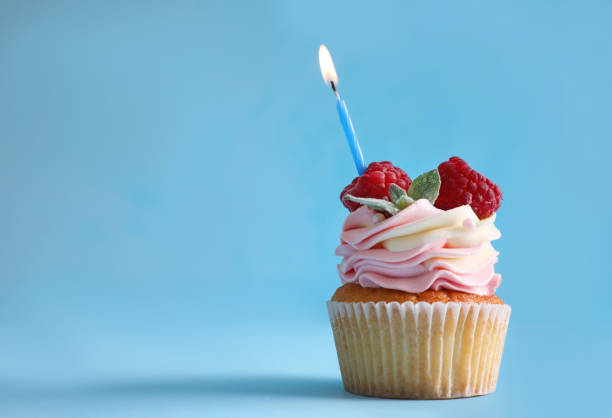 istock Delicious birthday cupcake with raspberries and burning candle on light blue background. Space for text 1353098859