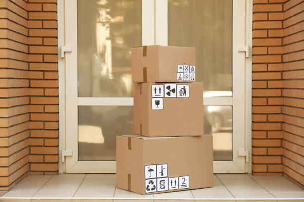 istock Cardboard boxes with different packaging symbols on floor near entrance. Parcel delivery 1353098888