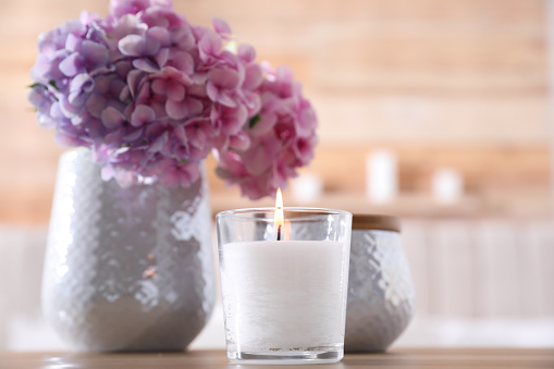 Burning candle and beautiful flowers on table indoors