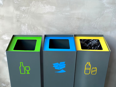 Group of plastic trash cans whit multicolored lid. Green bushes in the background.