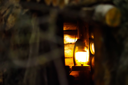 Old rusty kerosene lantern hanging in old wooden hut. Branches in a dark forest, horror, eerie and spooky atmosphere