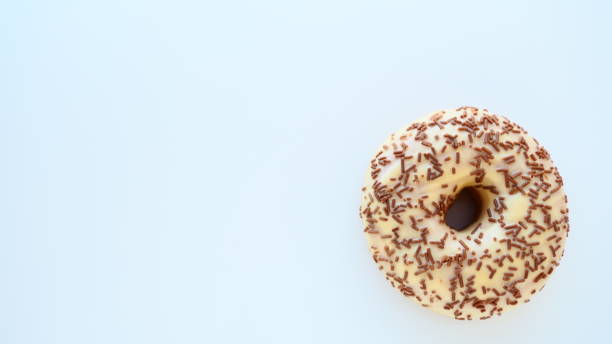 istock Doughnut close-up on white or gray background. Delicious cake covered with vanilla icing and chocolate sprinkles. High-calorie breakfast or snack. Sweet dessert with vanilla and chocolate, donut or dough. 1353122768