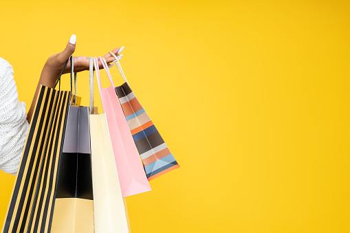 Shopping sale. Shopaholic lifestyle. Black Friday. Closeup of African woman hand holding paper bags isolated on orange copy space background.