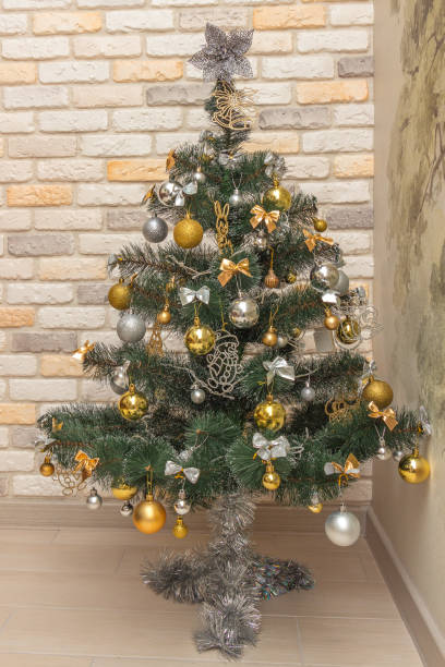 istock Decorated Christmas tree with the gold and silver baubles, multi-colored bows, animals, bells, lit garlands against the decorative brick wall background. Winter holidays concept 1353123139