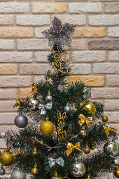 istock Decorated Christmas tree with the gold and silver baubles, multi-colored bows, animals, bells, lit garlands against the decorative brick wall background. Winter holidays concept 1353123151