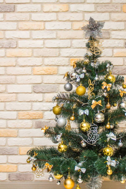 istock Decorated Christmas tree with the gold and silver baubles, multi-colored bows, animals, bells, lit garlands against the decorative brick wall background. Winter holidays concept 1353123163