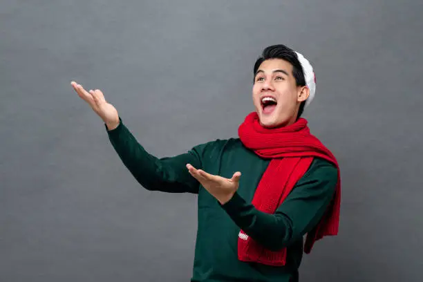 Photo of Studio portrait of surprised Asian man wearing a christmas themed attire with his arms raised