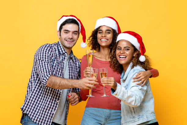 gruppo di tre amici diversi eccitati che celebrano il natale bevendo champagne insieme sullo sfondo giallo dello studio - clang foto e immagini stock