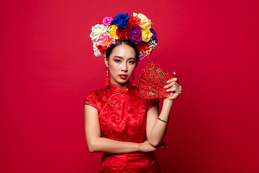 Gorgeous Asian woman in traditional oriental costume holding red envelopes or Ang Pao in isolated background for Chinese new year concepts, foreign text translates as great luck great profit