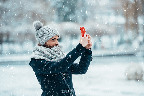 Woman taking selfie with a smartphone and wearing scarf and a a hat on a cold winter day