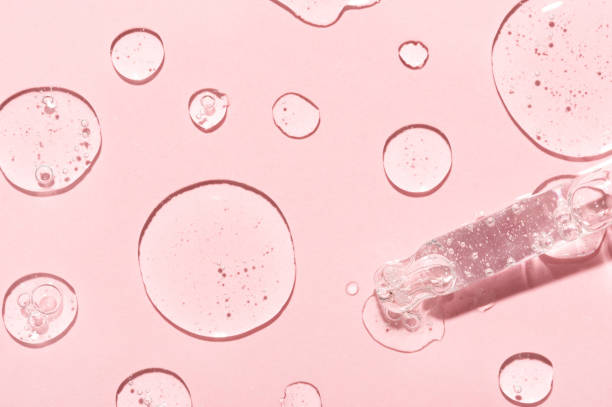 gotas de emulsão anti-envelhecimento e pipeta de vidro em rosa claro - oil slick pouring chemical oil - fotografias e filmes do acervo