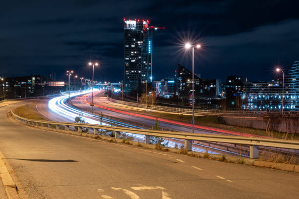 istock Bypassing vehicles casting light trails on the highway with modern city district in the background during the night. 1353130894