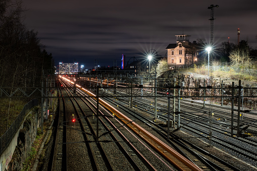 Helsinki / Finland - NOVEMBER 13, 2021: Bypassing trains casting light trails on the rail tracks with beautiful city skyline on the background.