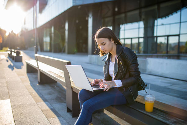 istock Young cheerful woman student using laptop outdoors 1353134197