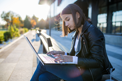 Young cheerful woman student using laptop outdoors