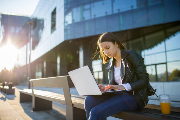 istock Young cheerful woman student using laptop outdoors 1353134230