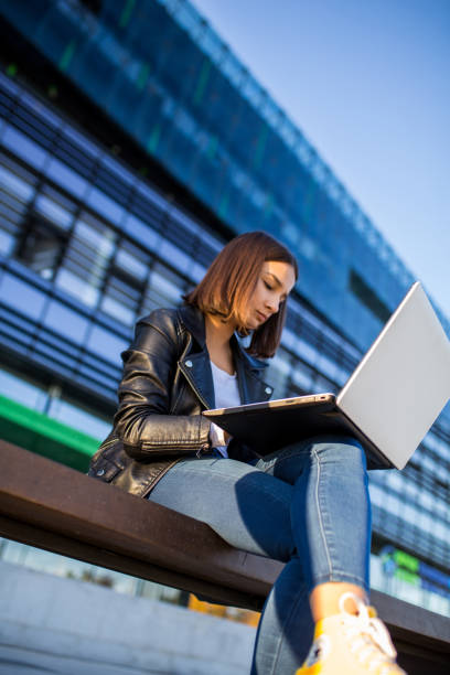 istock Young cheerful woman student using laptop outdoors 1353134257