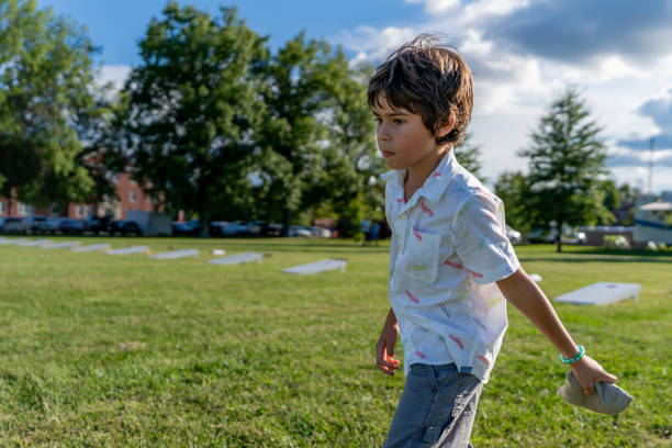 młody chłopiec podrzuca worki z fasolą na deskę z kukurydzy podczas letniego popołudnia z chmurami na niebie. - cornhole leisure games outdoors color image zdjęcia i obrazy z banku zdjęć