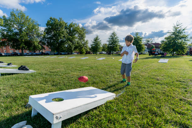 어린 소년이 여름 오후에 옥수수 구멍 보드에 콩 가방을 던지며 하늘에 구름이 있습니다. - cornhole leisure games outdoors color image 뉴스 사진 이미지