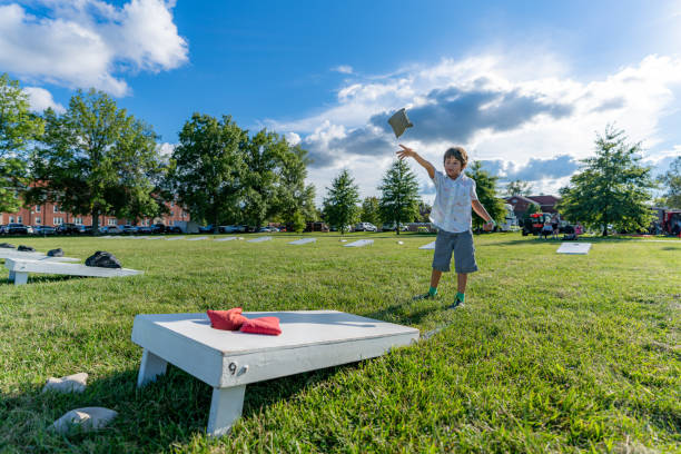 어린 소년이 여름 오후에 옥수수 구멍 보드에 콩 가방을 던지며 하늘에 구름이 있습니다. - cornhole leisure games outdoors color image 뉴스 사진 이미지