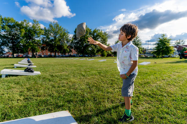 młody chłopiec podrzuca worki z fasolą na deskę z kukurydzy podczas letniego popołudnia z chmurami na niebie. - cornhole leisure games outdoors color image zdjęcia i obrazy z banku zdjęć