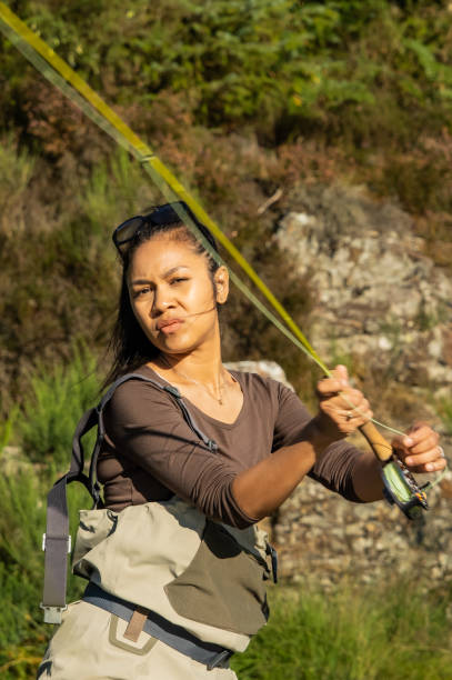 A young asian female fly fishing on a river on a summers evening A young asian female fly fishing on a river on a summers evening fly fishing scotland stock pictures, royalty-free photos & images