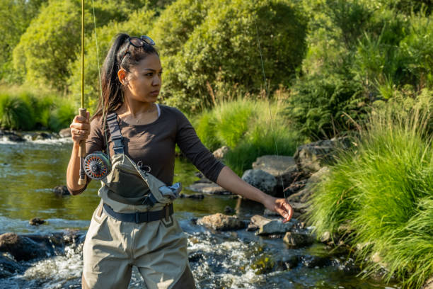 A young asian female standing fly fishing in a riffle on a river A young asian female standing fly fishing in a riffle on a river fly fishing scotland stock pictures, royalty-free photos & images