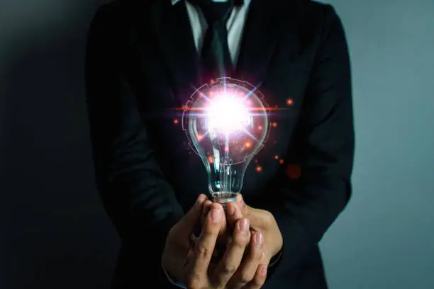 Hand of businessman holding light bulb, innovative technology. Mixed media, digital concepts.