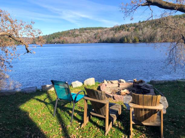A beautiful view of three chairs around a fire pit overlooking the Gatineau River with autumn foliage in the background, in Wakefield, Quebec, Canada. stock photo