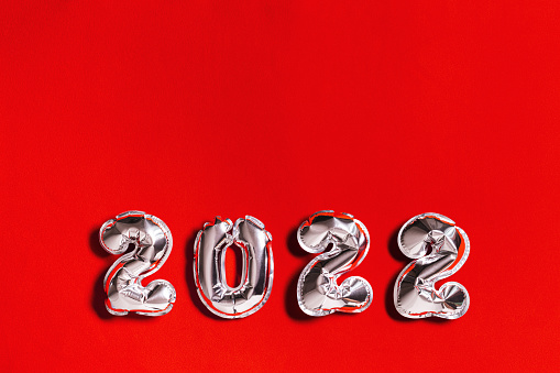 Silver balloons number 2022 New Year on red cloth background with copy space for congratulations. Bright layout for greeting card or invitation for new year party