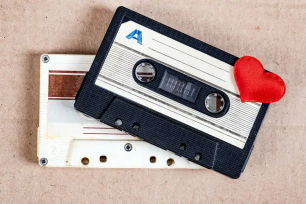 Two Old Audio Cassettes with a Red Heart on the Paper Background closeup