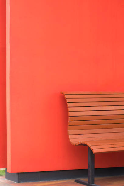Side view of empty wooden bench on red wall in vertical frame, minimal background design concept
