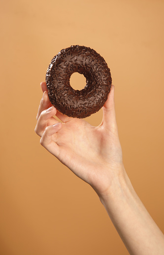 female hand holding tasty chocolate donut isolated on brown background
