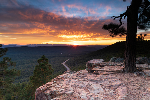 Sunset from the top of Mogollan Rim above Payson, Arizona. Pine forest and highway below; Sunburst, brillian orange clouds and blue sky in distance.