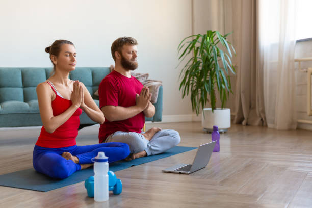 casal meditando em casa com tutorial de yoga online - middle human age couple women - fotografias e filmes do acervo