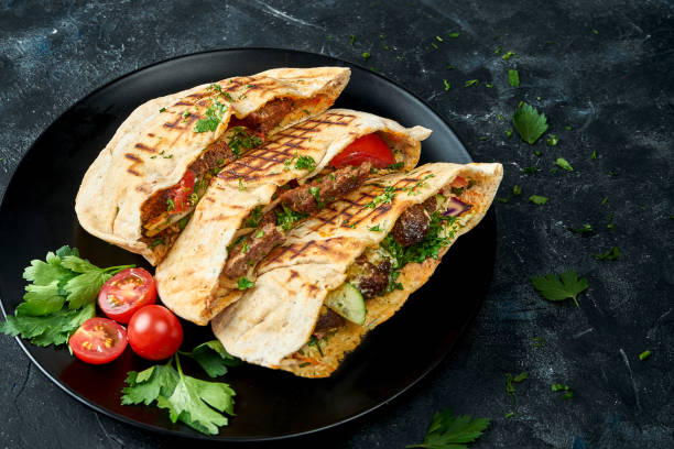 istock Three pita bread with vegetables, chicken and beef in a black plate on a dark background 1353182194
